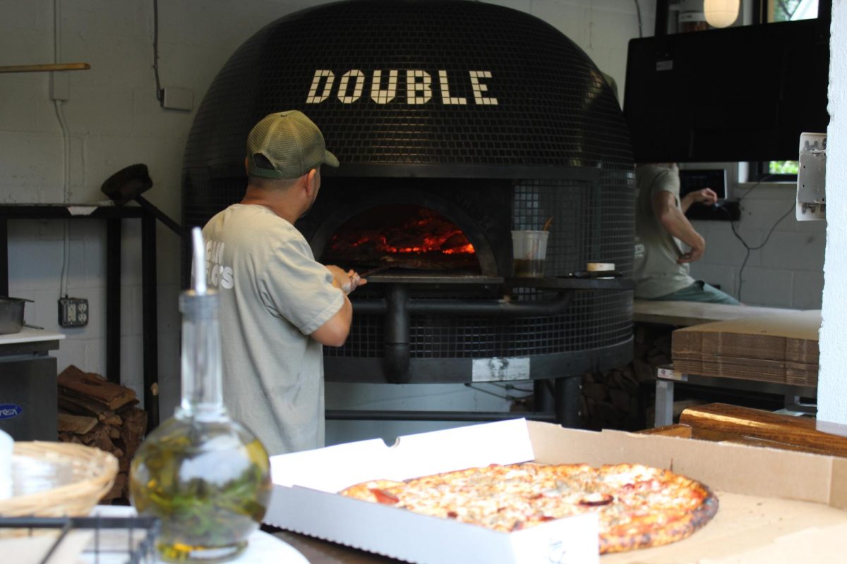 An employee carefully slides the perfectly topped pizza into the pizza oven.