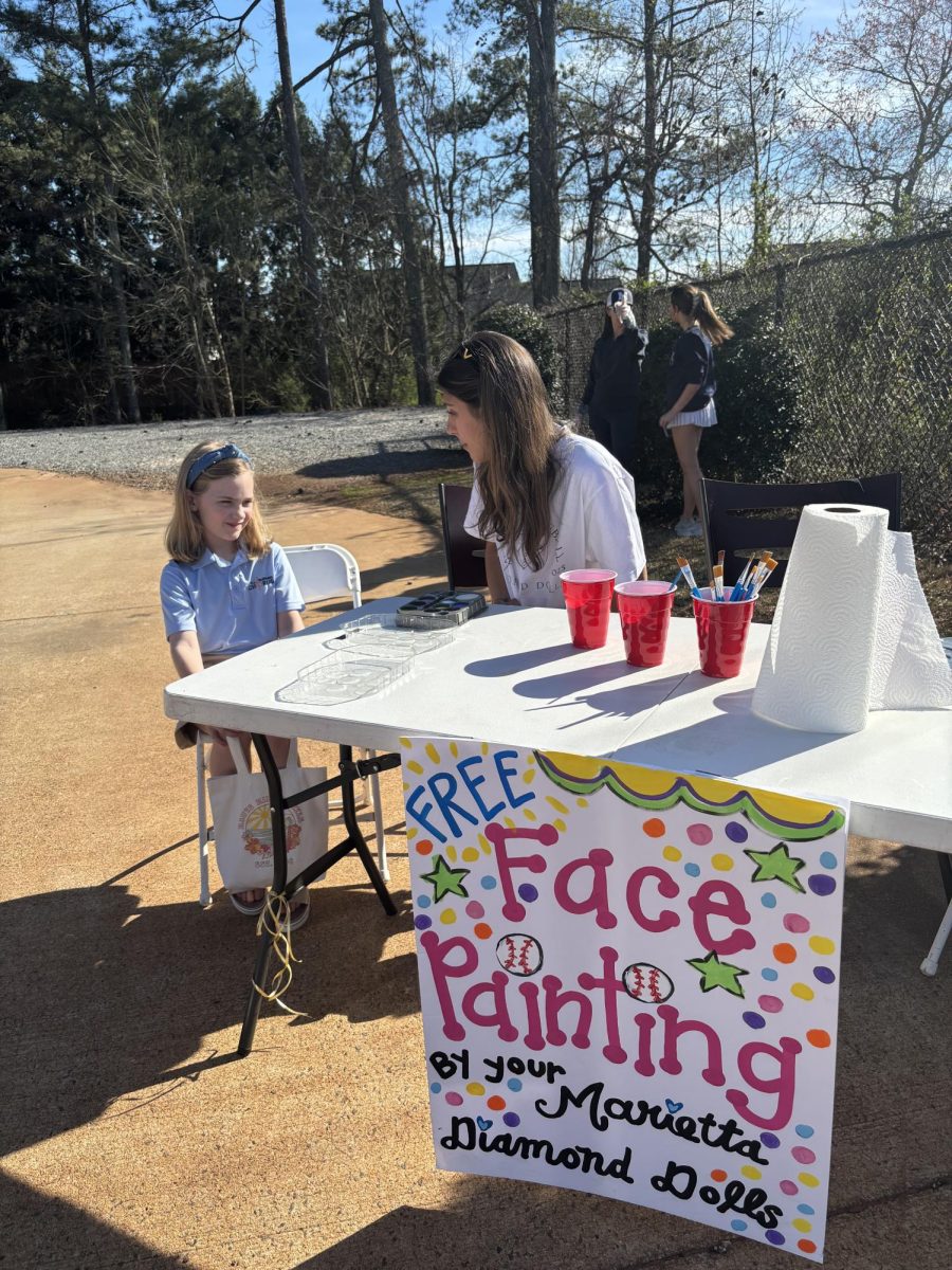 Senior Diamond Doll Gabby Stanley prepares to paint Charlotte Heisler's face during A.L. Burrss elementary night.